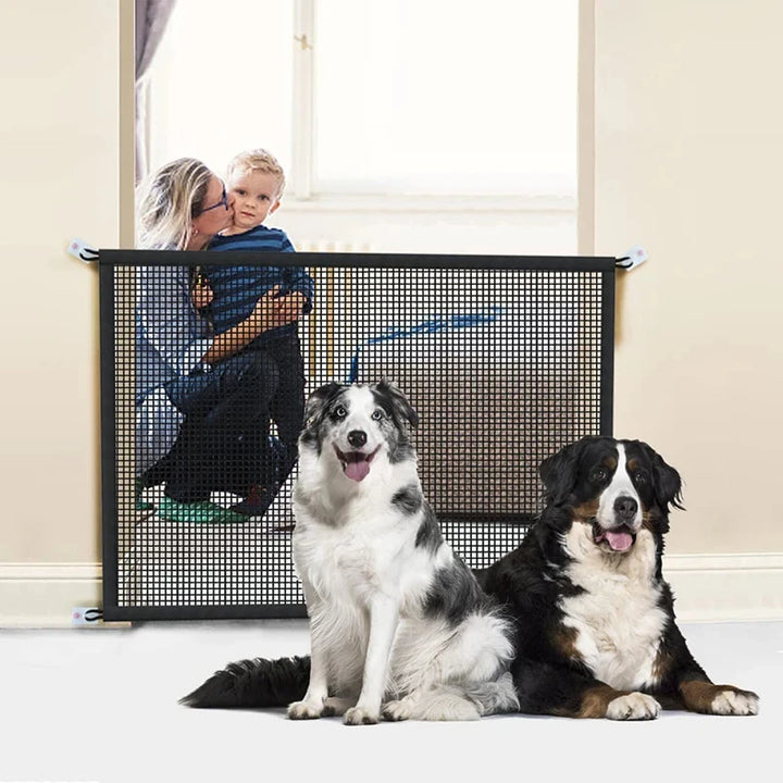 Two dogs sitting in front of a pet gate with a child and adult standing behind it.
