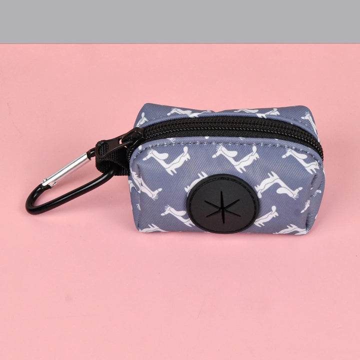 Small blue Dog Poop Bag Holder with white dog pattern, black zipper, and carabiner on a pink background