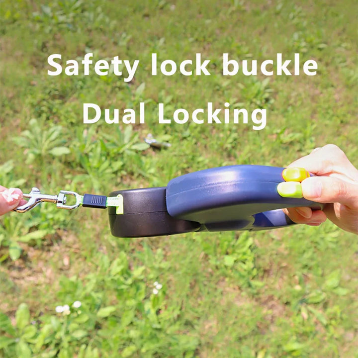 Person holding a retractable double dog leash  with a safety lock buckle labeled 'Dual Locking' against a grassy background.