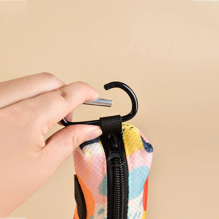 Hand holding a colorful Dog Poop Bag Holder with a black carabiner on a beige background