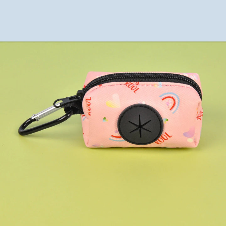 Pink Dog Poop Bag Holder with colorful patterns and a carabiner on a green background